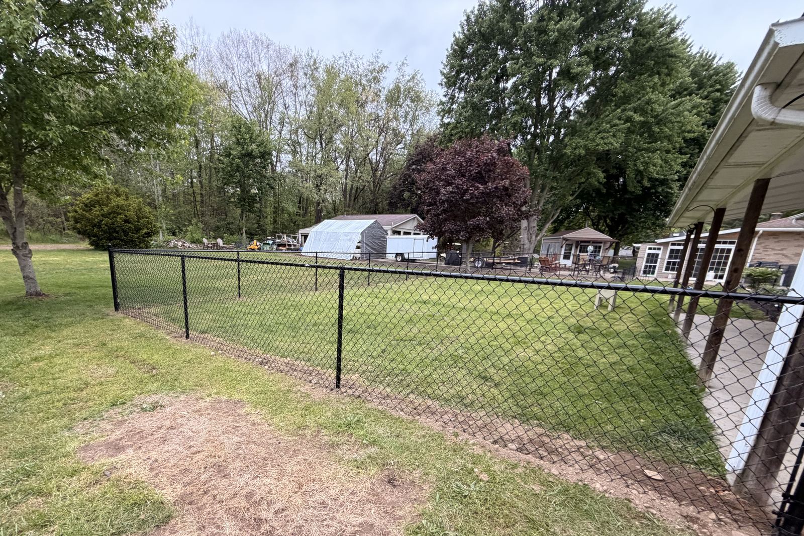 Black vinyl-coated chain link fence enclosing a residential backyard lawn, installed by Warrior Barriers