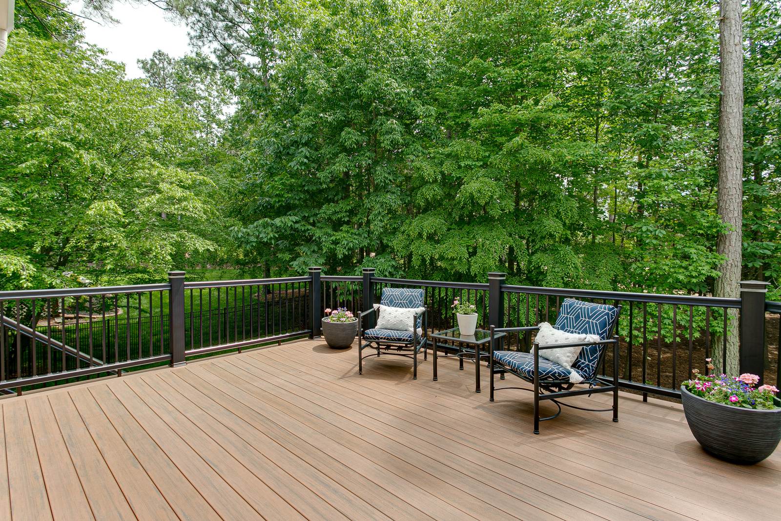 Composite deck with black aluminum railing, patio chairs, and a view of the wooded backyard
