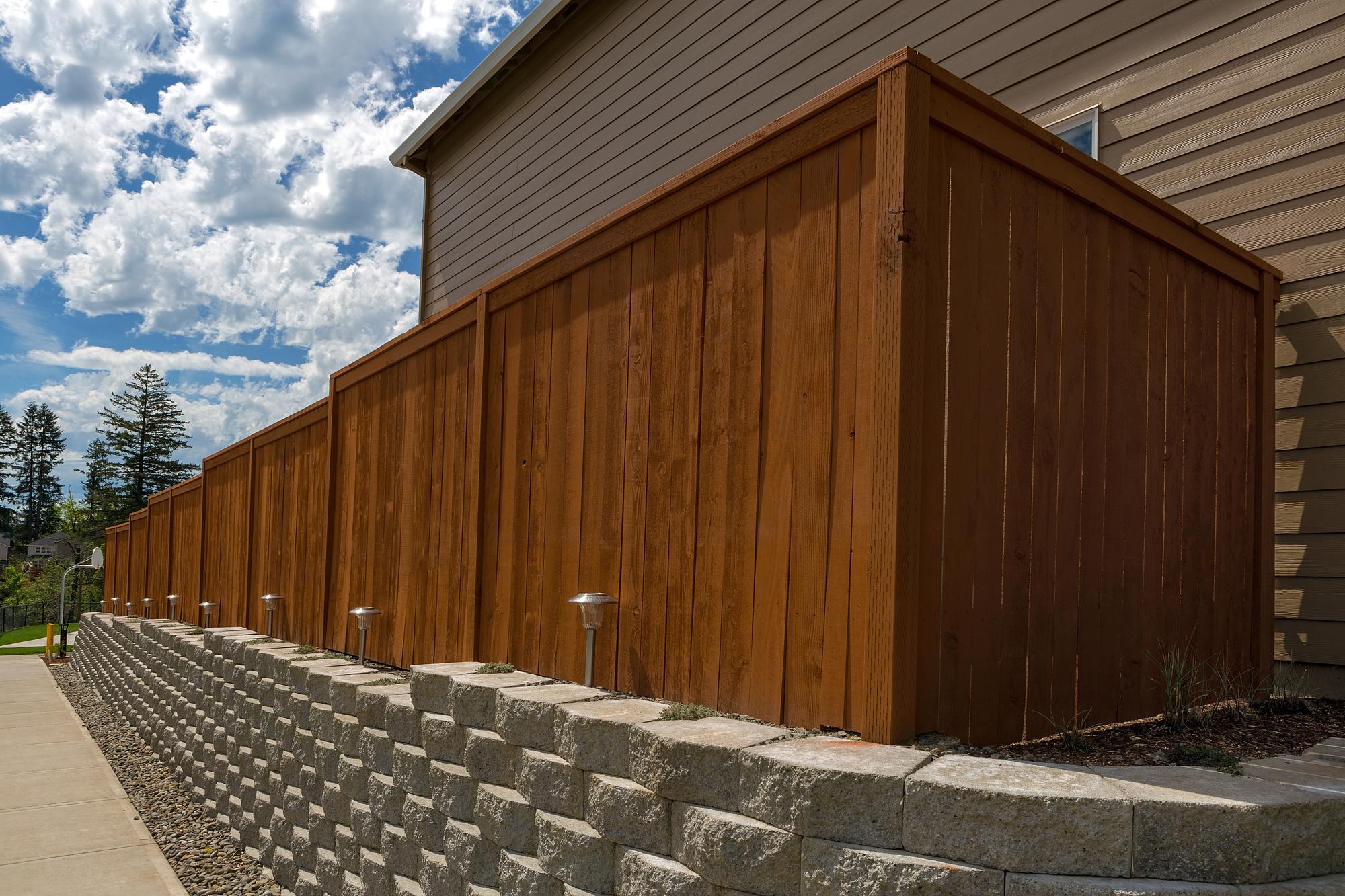 Stained wood privacy fence built on top of a stone block retaining wall beside a home in Tuscarawas County, Ohio