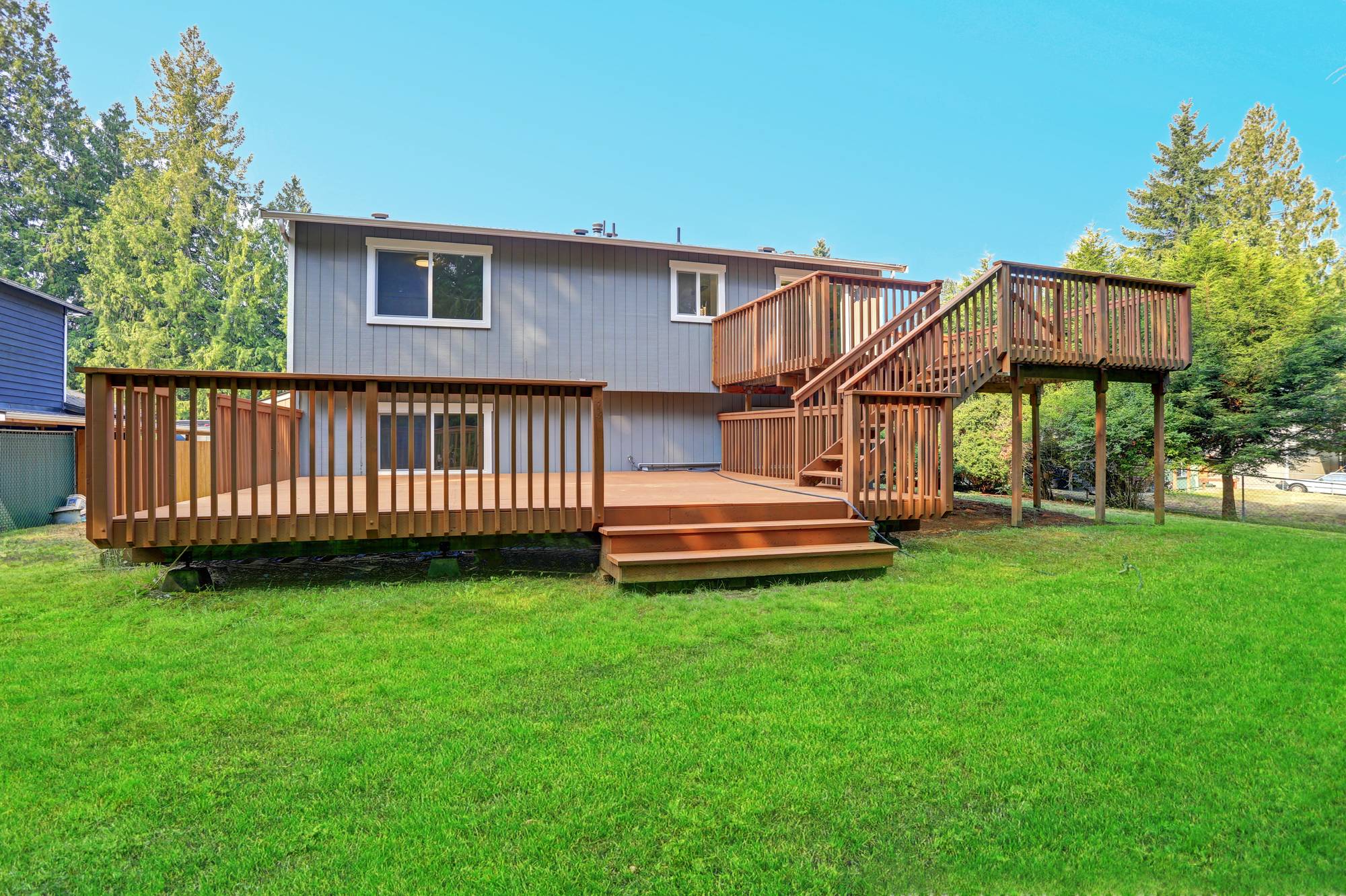 Large two-level stained wood deck with stairs behind a gray house