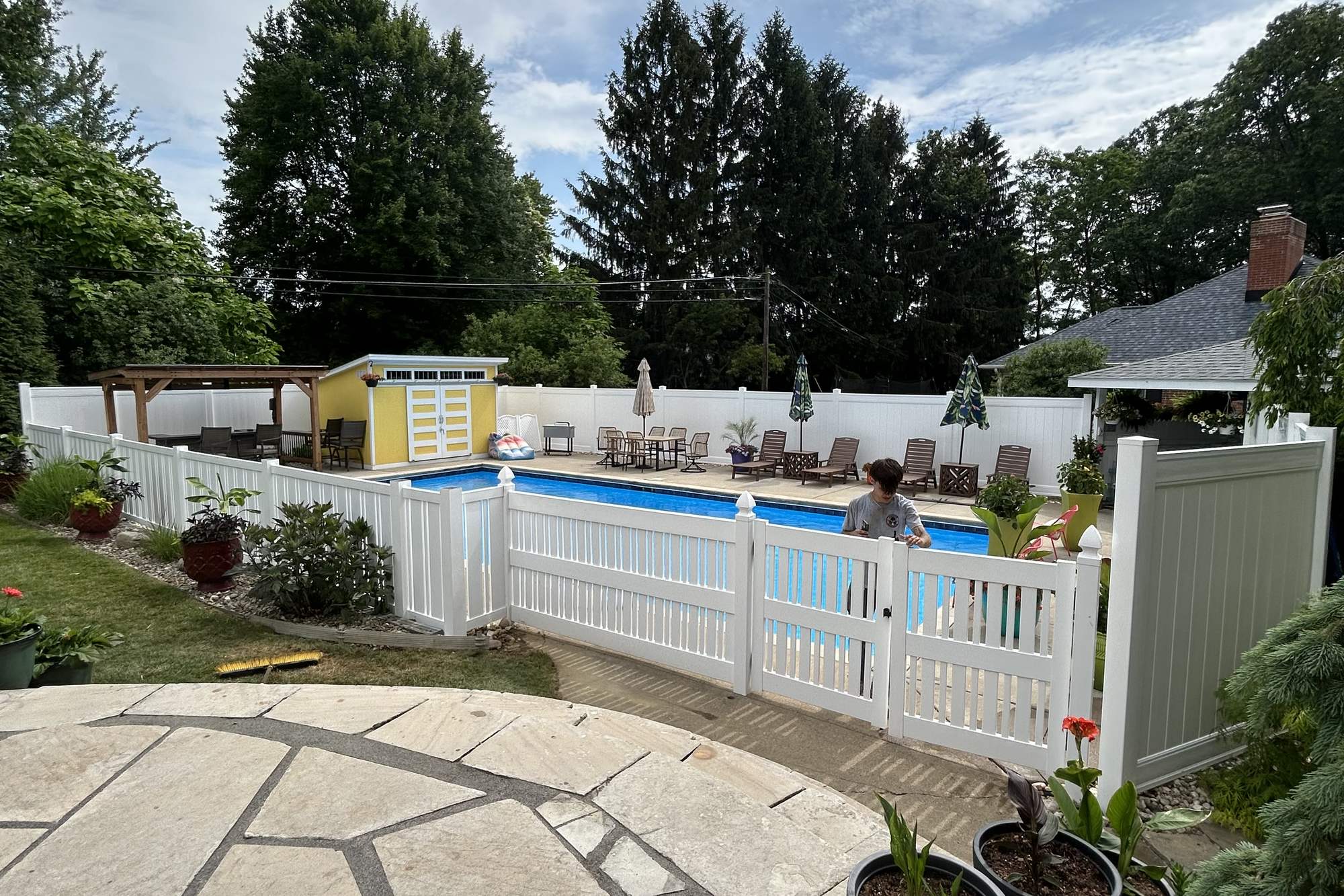White vinyl fence around an in-ground pool, with picket-style pool sections, a gate, and privacy sections behind, installed by Warrior Barriers
