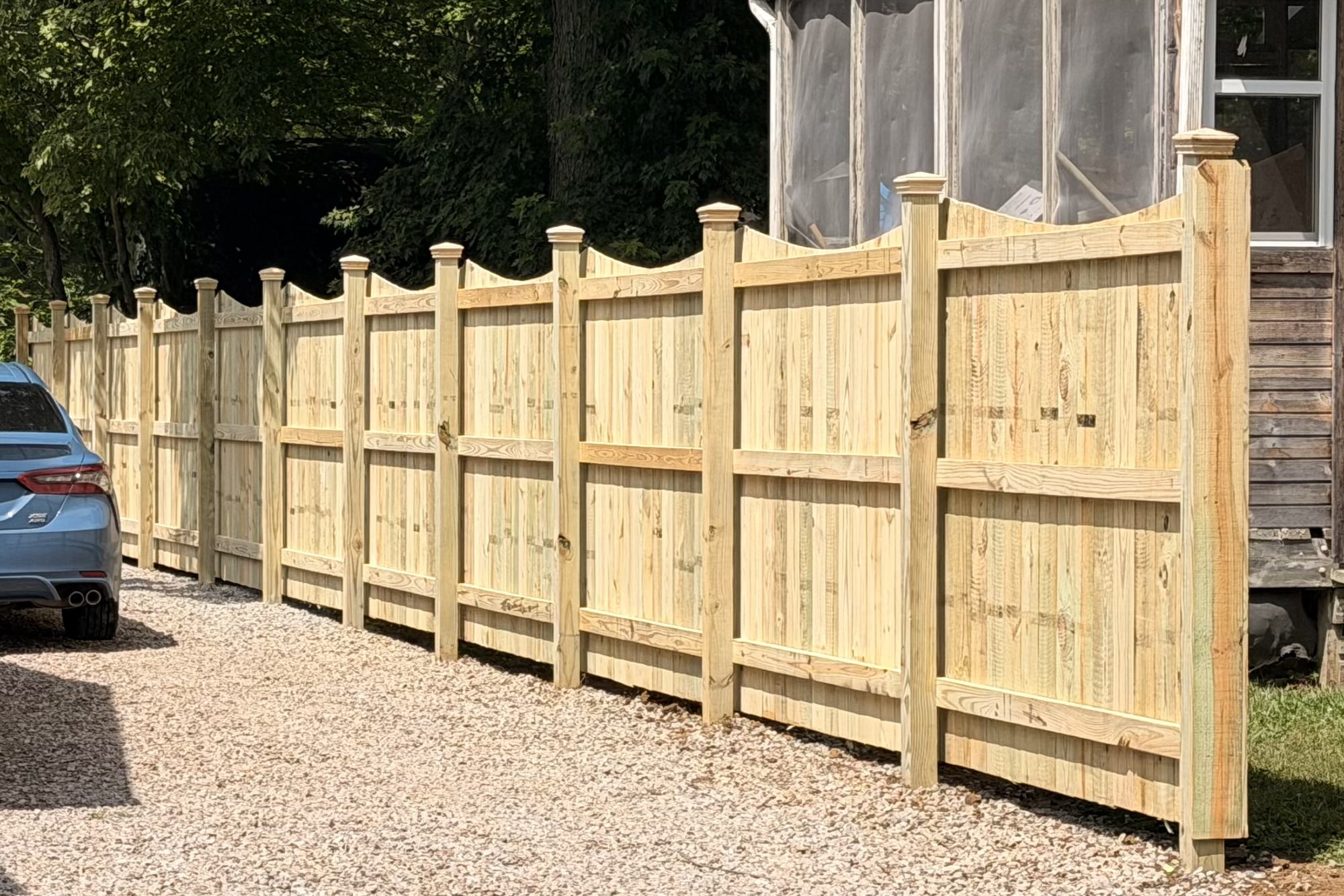 Wood privacy fence with capped posts along a gravel driveway, installed by Warrior Barriers