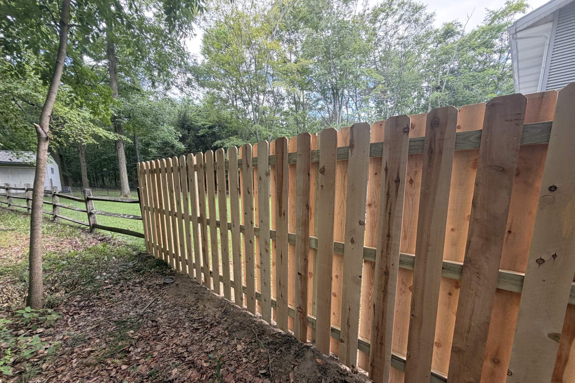 Wood shadowbox fence with alternating boards in a wooded backyard